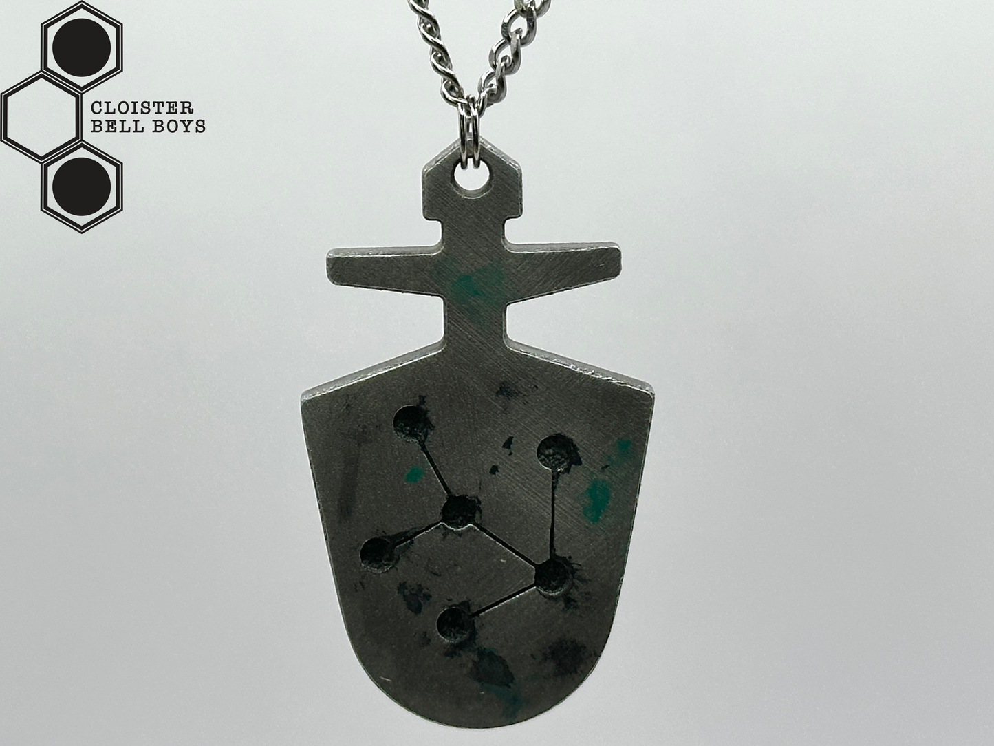 The back of a McGann Key, a pendant with geometric design on a gray background, branded 'Cloister Bell Boys'.