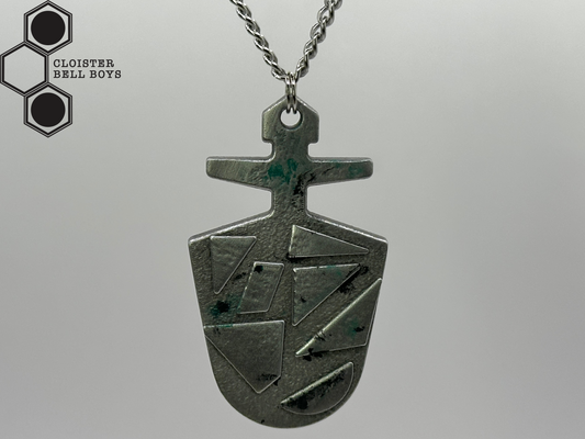 A McGann Key, a metallic pendant with geometric design, on a gray background, hanging from a chain, branded 'Cloister Bell Boys'.