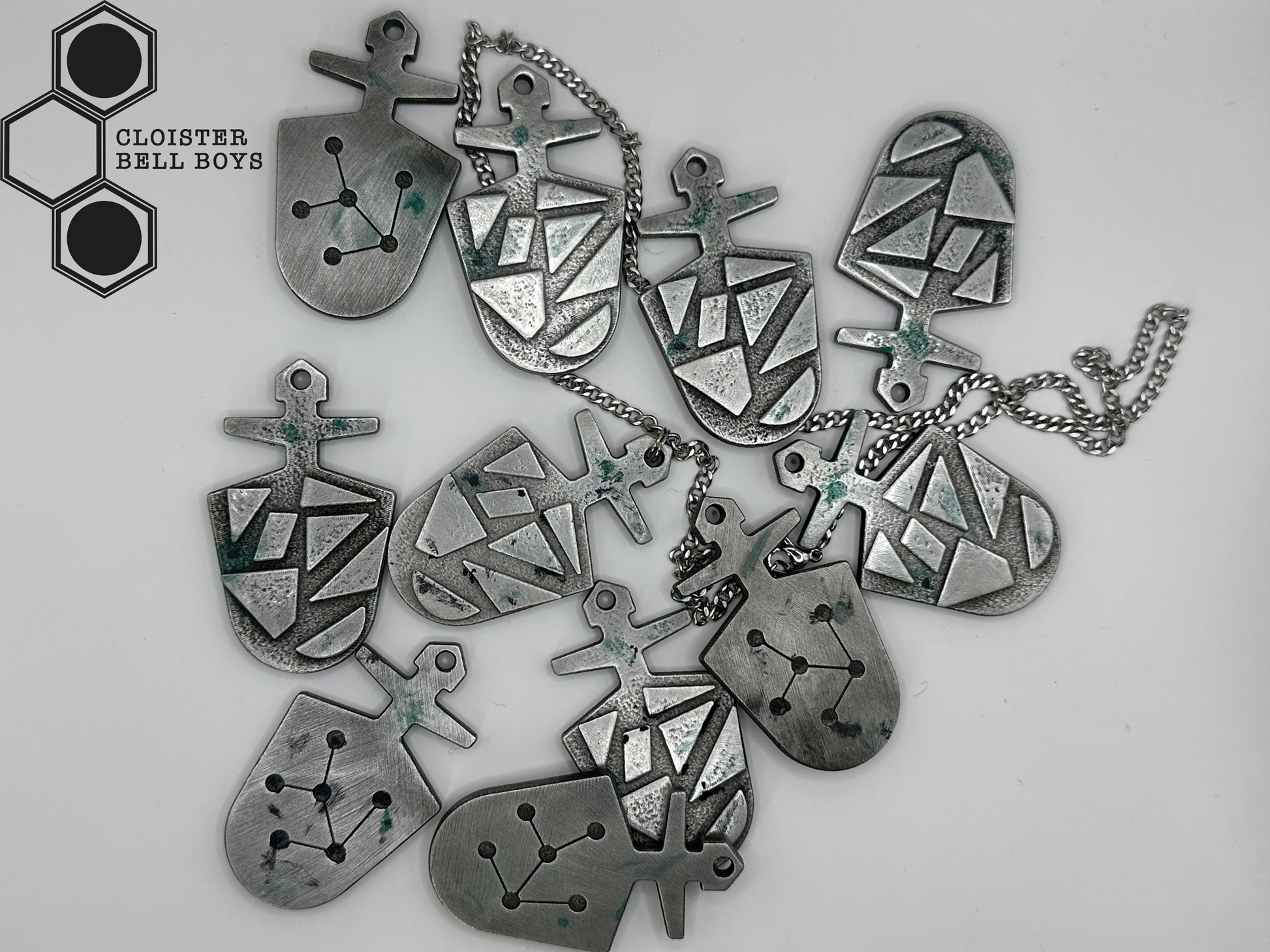 Collection of "McGann Keys", silver pendants on a white background with 'Cloister Bell Boys' branding. Some are attached to chains and some are not. 