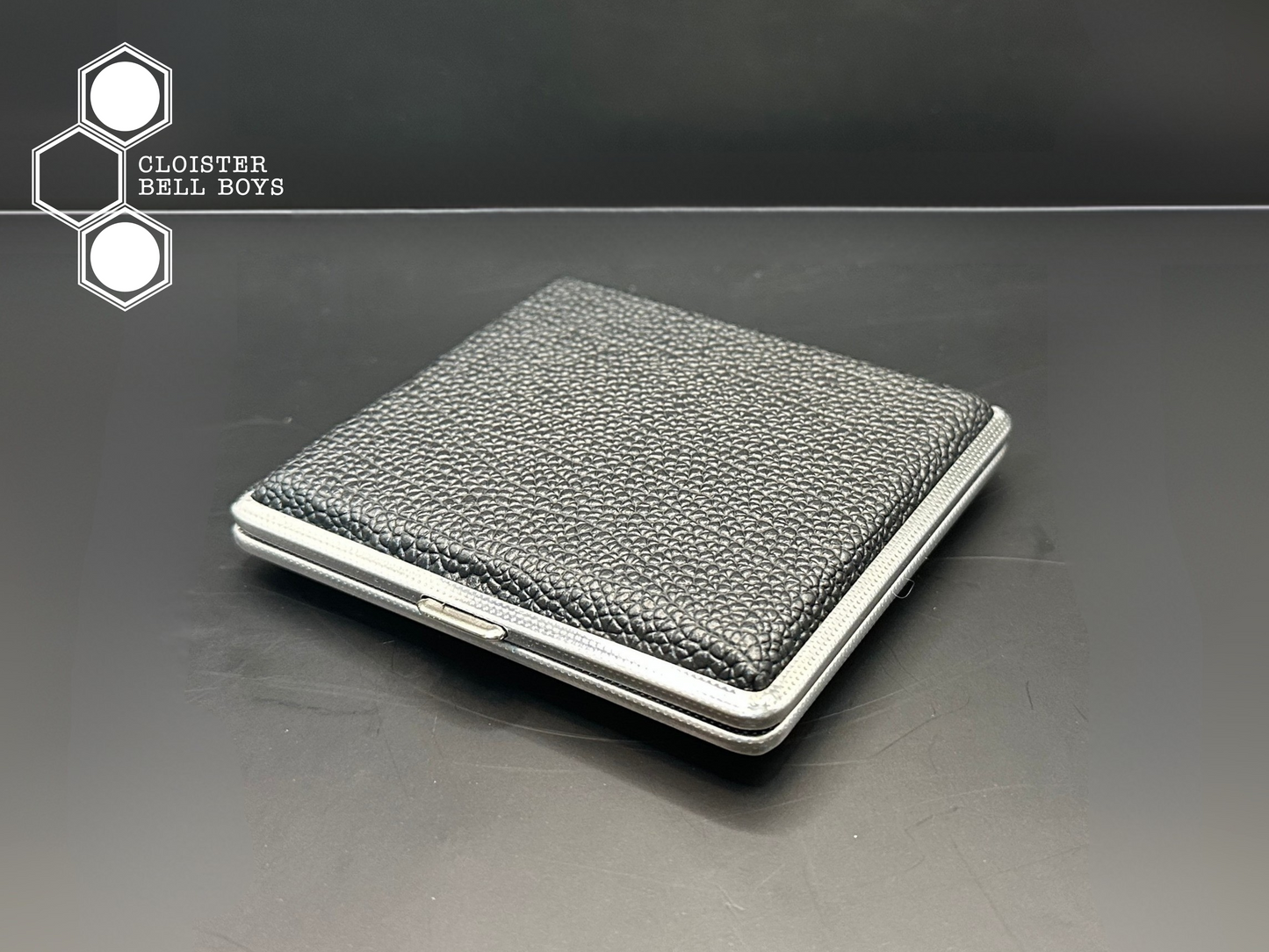 Black leather and metal cigarette case on a black surface with 'Cloister Bell Boys' branding.