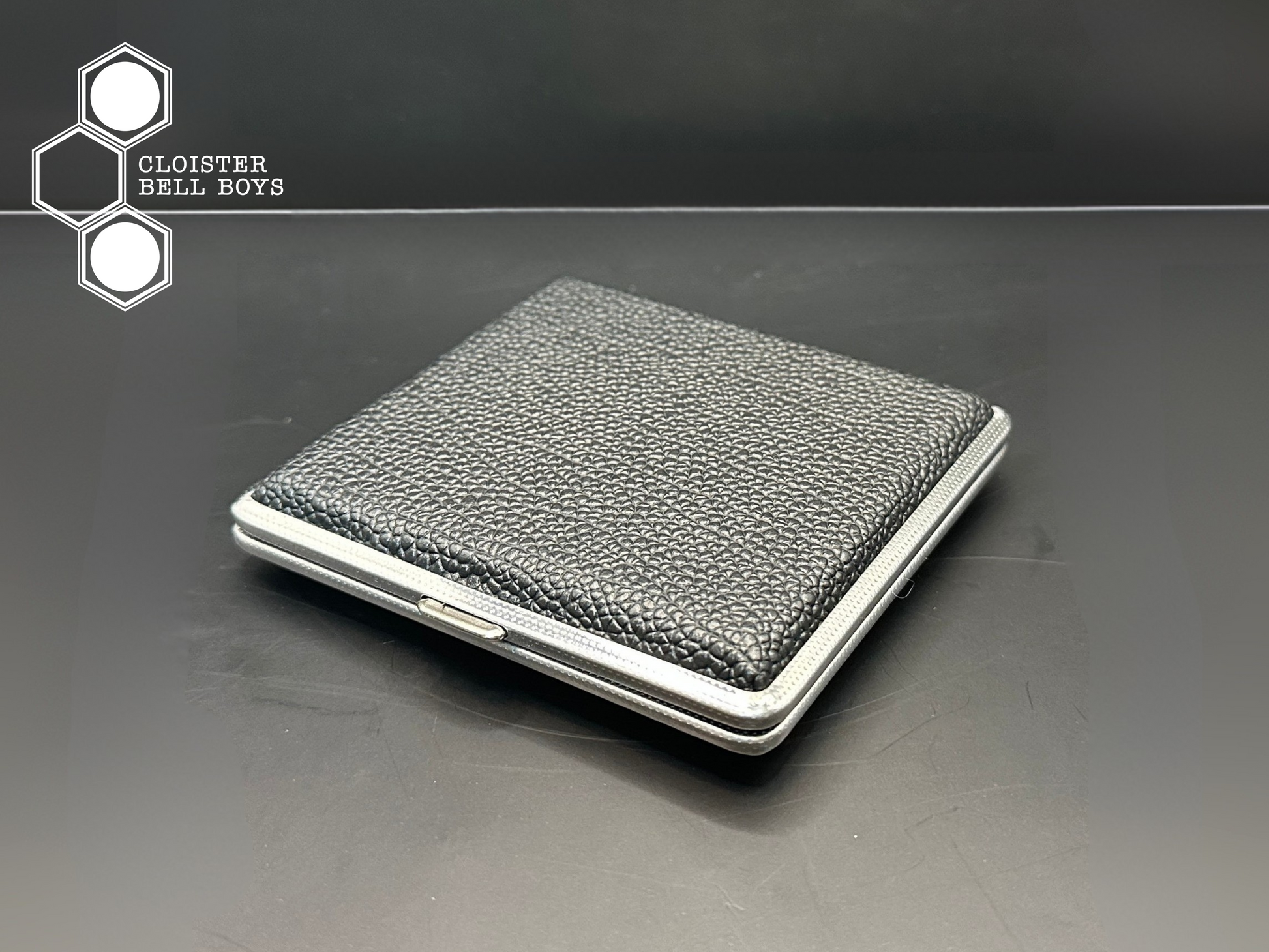 Black leather and metal cigarette case on a black surface with 'Cloister Bell Boys' branding.