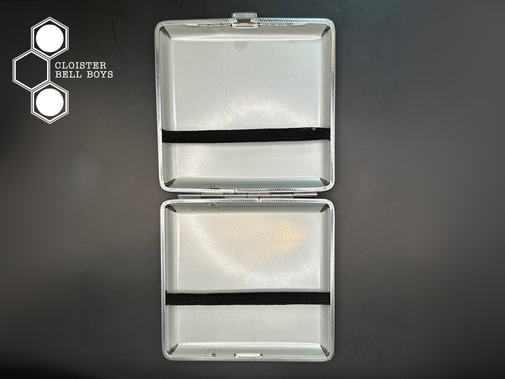 Silver metal cigarette case with black band on a dark background