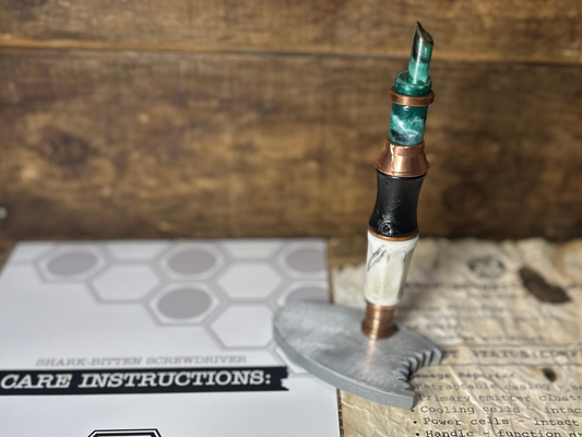 Shark-Bitten Screwdriver in a decorative stand on a wooden surface with care instructions visible.